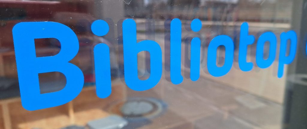 Blaues Schild mit der Aufschrift 'Bibliotop' an einem Fenster.