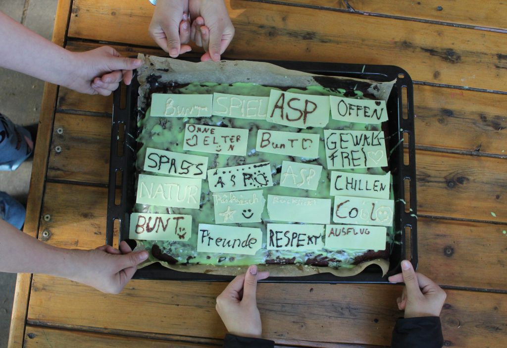 Beim Verzieren zum Tag der gewaltfreien Erziehung kleben Kinder Esspapier-Schilder auf grünem Zuckerguss für Gewaltfreiheit am ASP.