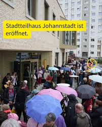 Vor dem Stadtteilhaus Johannstadt drängen sich viele Menschen mit bunten Regenschirmen bei der Eröffnung an einem grauen, regnerischen Tag.
